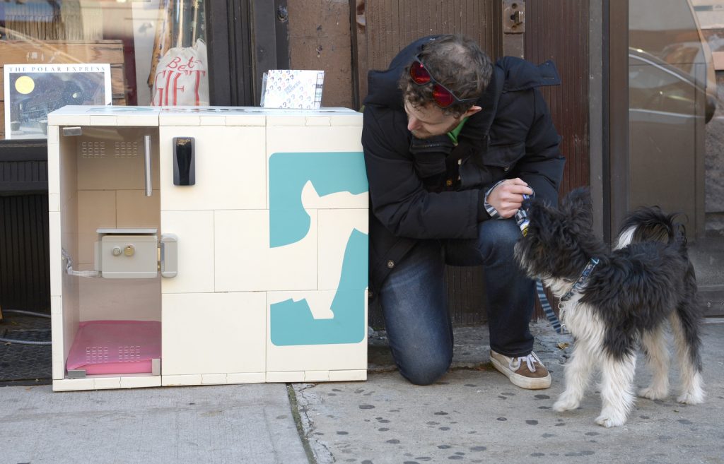 Dog Parker. PICTURED Eric Abis pictured with his pouch "Bernie" outside Fort Greene General Store at 218 Dekalb avenue (he plans to use it in near future). Pet owners who are averse to tying their dogs outdoors while running errands have a novel option in Brooklyn: "parking" their dogs in sidewalk containers outside retail stores. The "dog parker" program, which launched as a pilot in Brooklyn last month, is run through an app that charges 20 cents per minute - or $12 for an hour. Users can call dibs on an insulated kennel 15 minutes ahead of time in order to buy groceries or enter other stores where dogs are forbidden -- without having to walk all the way home first. The containers are lockable via radio frequency, monitored by web cams and temperature controlled unless the mercury dips below freezing. The firm launched a 10 kennel pilot in October with 50 users. It's not clear if the pilot had expanded yet or is still ongoing with two locations in Fort Greene, Brooklyn NYC. First outside Baguetteaboutit coffe shop at 270 Vanderbilt avenue and the other block away Fort Greene General Store at 218 Dekalb avenue.